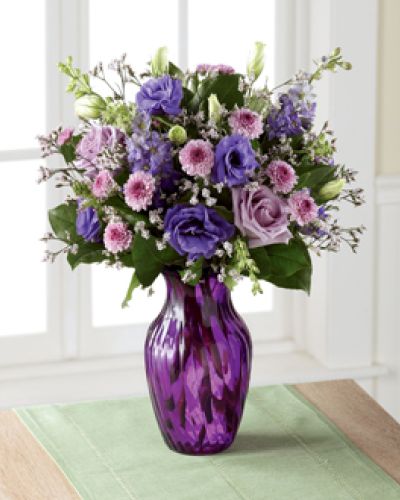 Elegant and chic, this flower bouquet is laced in lavender to send your love, kindness, and gratitude to your recipient this spring season. Lavender roses and purple double lisianthus flaunt their twilight inspired beauty, mingling amongst purple button poms, purple larkspur, pink limonium, and lush greens, presented in a purple swirled glass vase. The perfect thank you, birthday, or Mother's Day gift.