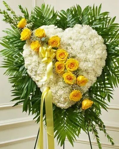 This solid heart standing spray, accented with a slash of beautiful yellow roses, is a loving symbol of your sympathy and support. White carnations, yellow roses, baby's breath and more make up this solid heart with oasis in mache, tied to the wire easel with satin ribbon. Traditionally sent directly to the funeral home by family members or friends and displayed on a stand.