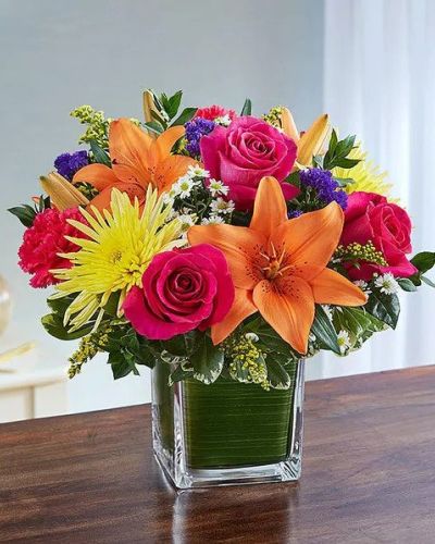 Send a beautiful expression of your sympathy with this cube vase arrangement. This bouquet features bright-toned blooms such as roses, lilies, spider mums, carnations, solidago, statice and monte casino accented with variegated pittosporum and myrtle. Appropriate for the service or for sending to the home or office of friends and family members.