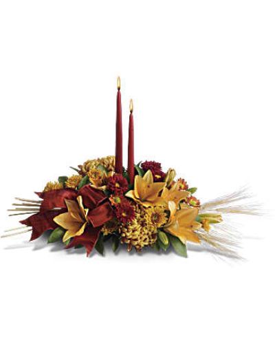 Add a graceful glow to your Thanksgiving dinner table or fall-decorated foyer with this warm, seasonal arrangement. Lilies, mums and asters are accented with sprays of wheat below glowing taper candles.
This classic Thanksgiving centerpiece features orange asiatic lilies, red matsumoto asters, bronze disbud mums, bronze daisies and bronze cushion mums.
Burgundy satin ribbon, stems of wheat, and two taper candles add seasonal sophistication.